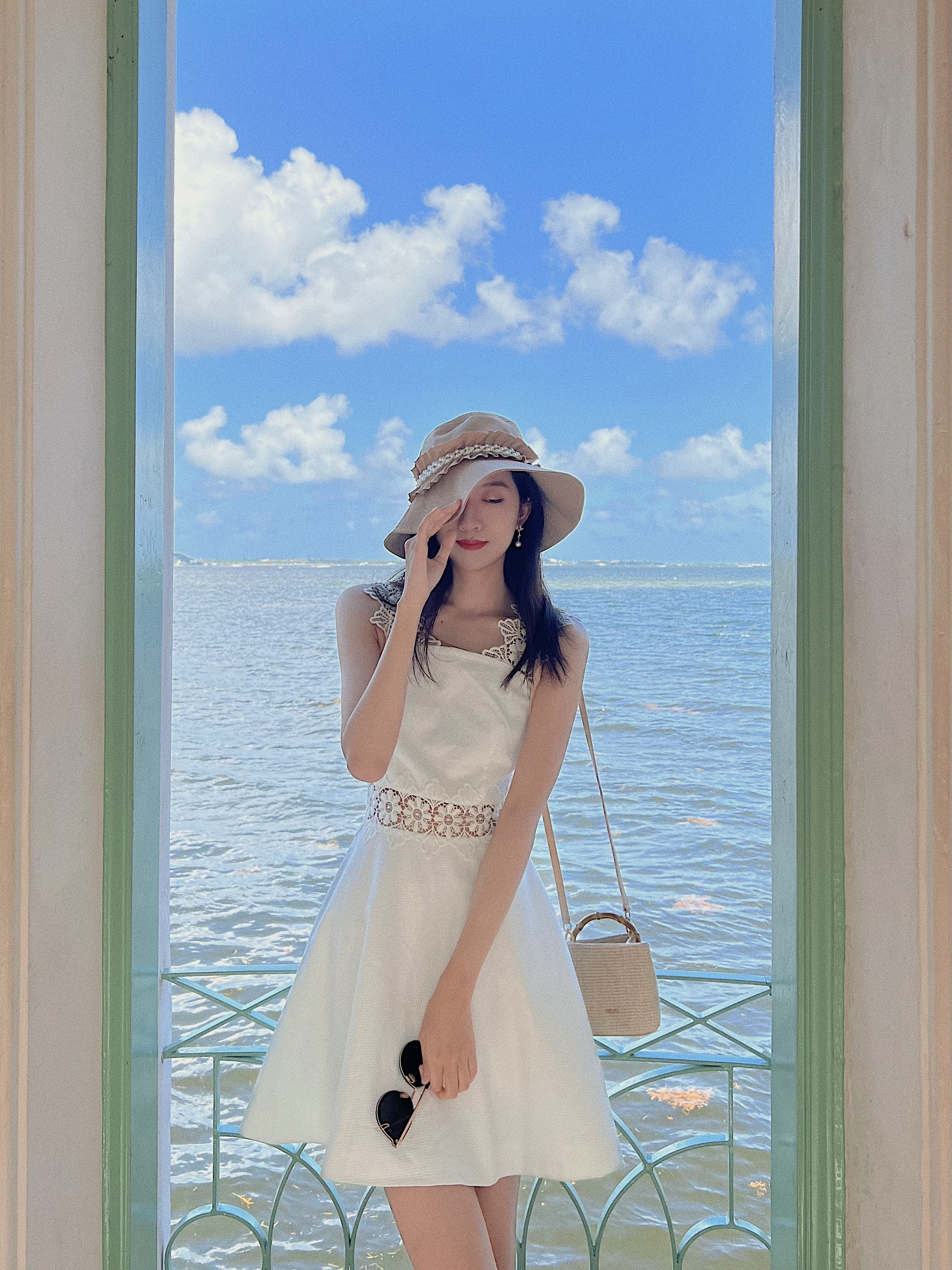 The girl standing in front of the sea, with the hat covering half of her face